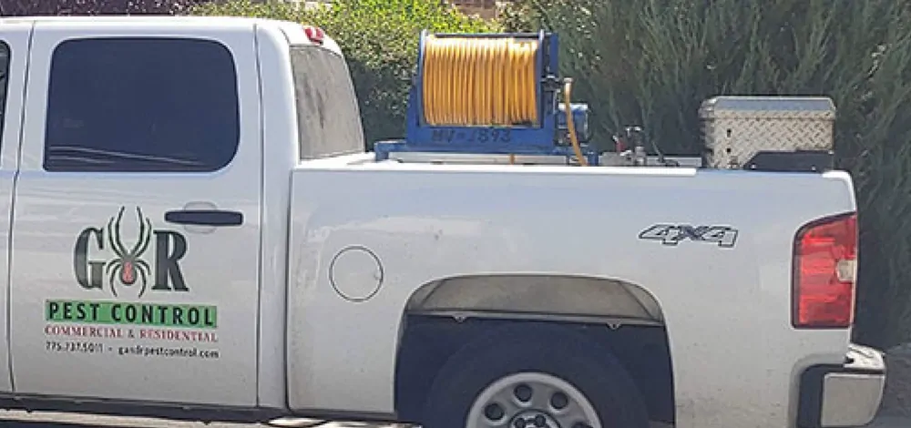 Door of G&R's white pickup: the G&R spider logo, PEST CONTROL, COMMERCIAL & RESIDENTIAL and the phone number, with a yellow hose reel in the bed.