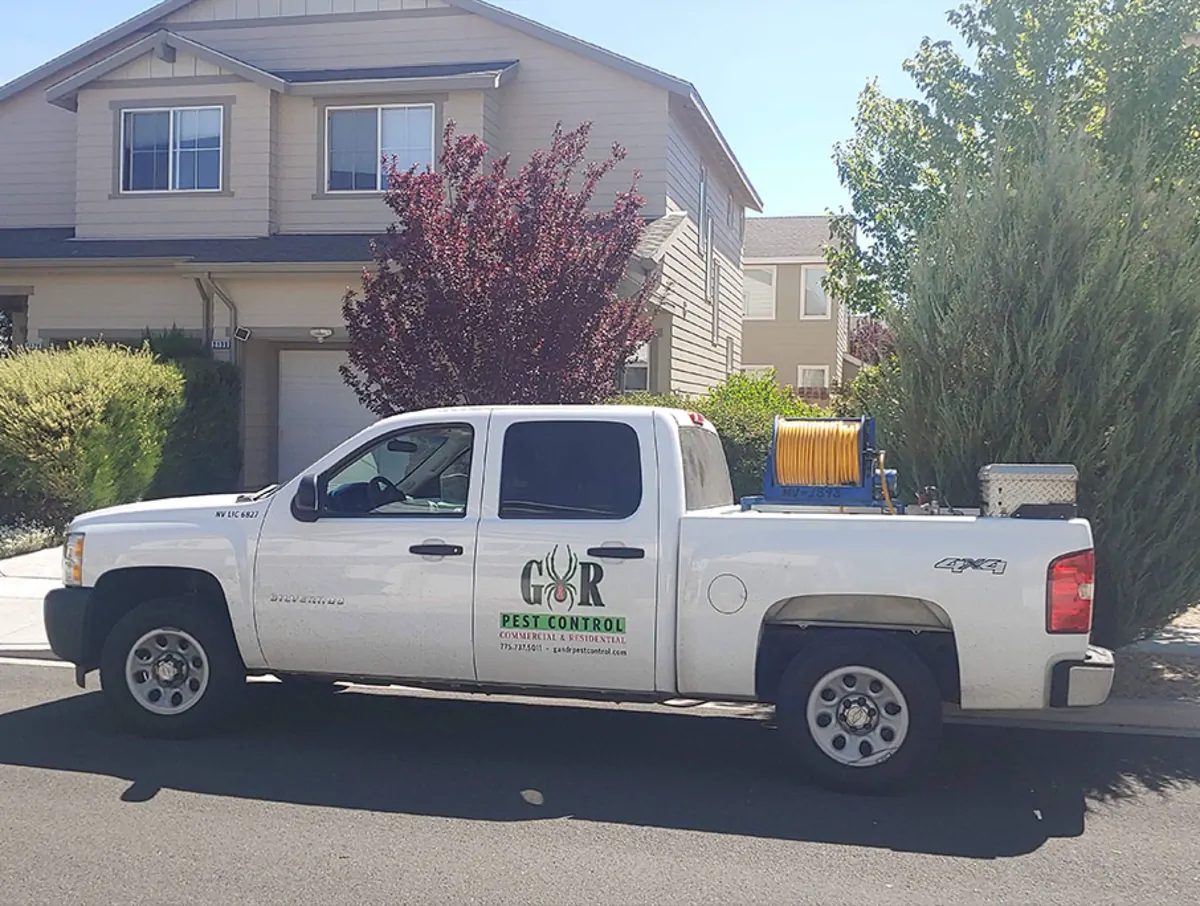 G&R's white pickup, with the company logo on the door and a hose reel and equipment box in the bed, parked outside a two-storey house with a garage, a purple-leaf tree and shrubs.